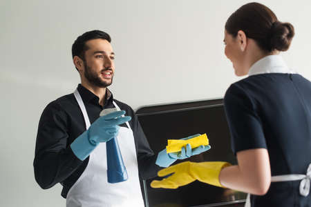 cheerful housekeeper in rubber gloves talking with blurred chambermaidの写真素材
