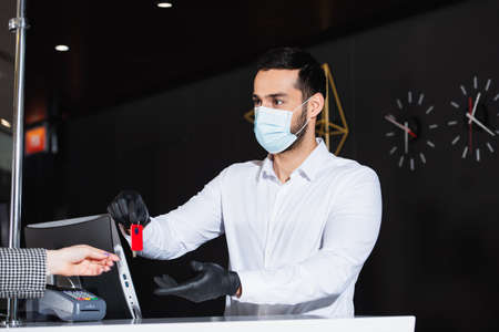 administrator in latex gloves and medical mask giving room key to guestの写真素材