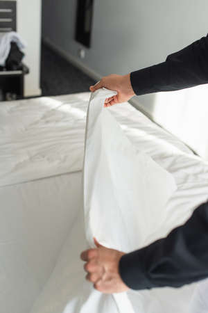 cropped view of housekeeper changing bedding in hotel room