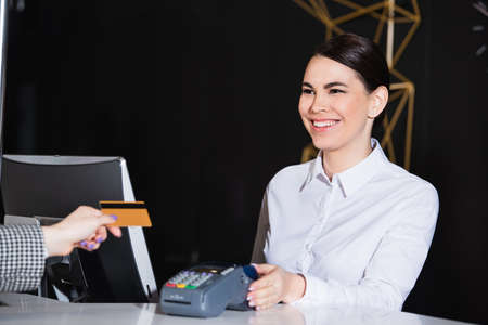 happy receptionist smiling near guest paying with credit card