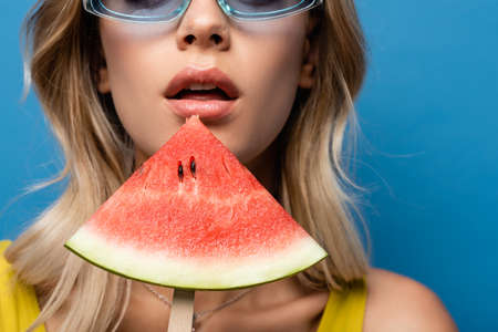 cropped view of young woman holding stick with watermelon isolated on blue