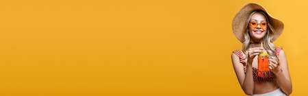 cheerful woman in straw hat and sunglasses holding alcohol cocktail isolated on yellow, bannerの写真素材