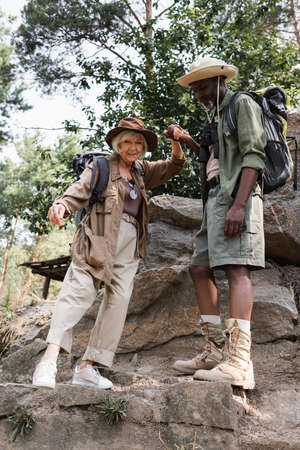 Interracial elderly hikers holding hands on stones in forestの写真素材