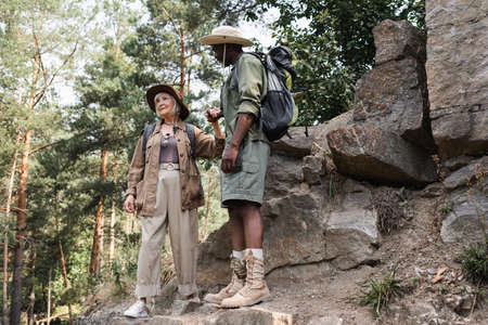 Elderly woman holding hand of african american husband near stones in forestの写真素材