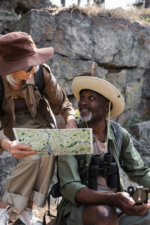 Smiling hiker holding map near african american husband with compass and rockの写真素材