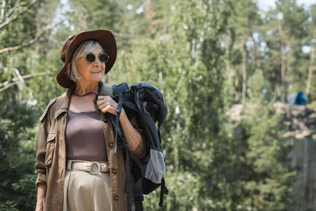 Senior tourist with backpack looking away in forestの写真素材