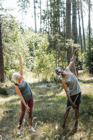 Smiling african american man in sportswear training near wife in forest