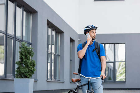 Arabian deliveryman with backpack talking on smartphone near buildingの写真素材