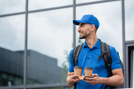 Side view of muslim deliveryman in cap holding paper cups outdoorsの写真素材