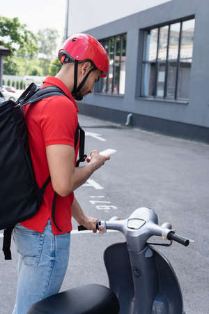 Arabian deliveryan in helmet using smartphone near scooter outdoorsの写真素材
