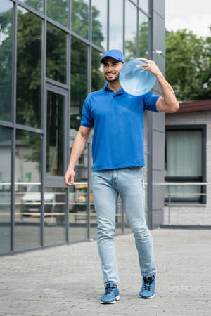 Cheerful muslim courier in uniform holding bottle of water outdoorsの写真素材