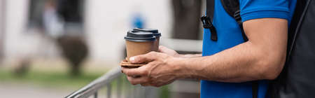 Cropped view of deliveryman with thermo backpack holding coffee to go outdoors, bannerの写真素材