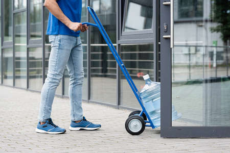 Cropped view of courier pulling cart with bottle of water near open door of buildingの写真素材