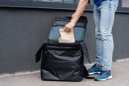Cropped view of deliveryman taking paper bag from thermo backpack outdoors