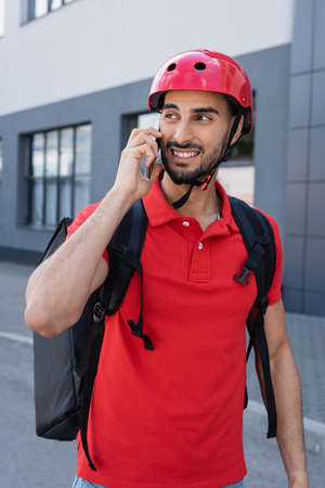 Smiling muslim courier in helmet talking on smartphone outdoorsの写真素材