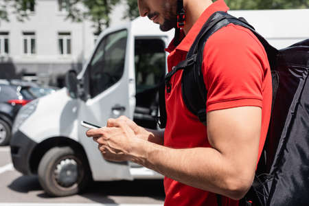Cropped view of courier with thermo backpack using smartphone outdoorsの写真素材