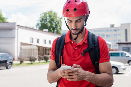 Arabian courier in helmet using smartphone on urban streetの写真素材