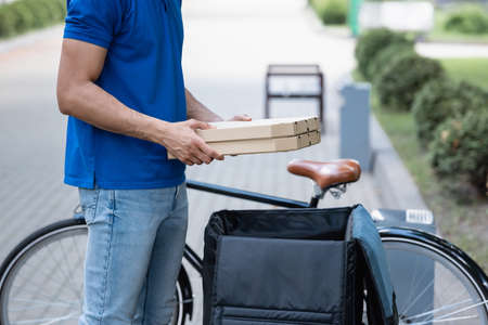 Cropped view of courier holding pizza boxes near open thrmo backpack and blurred bicycleの写真素材