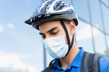 Young arabian deliveryman in bike helmet and medical mask outdoorsの写真素材