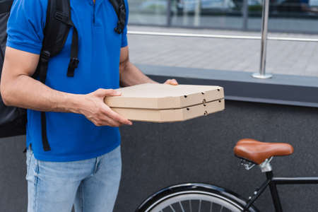 Cropped view of courier holding pizza boxes near blurred bicycle outdoorsの写真素材