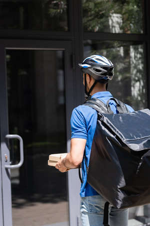 Young courier in safety helmet holding pizza boxes near door of buildingの写真素材