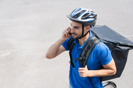 High angle view of smiling deliveryman with backpack talking on smartphone near bike outdoorsの写真素材