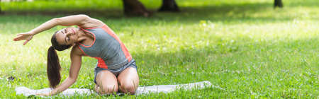 flexible and fit woman in sportswear stretching on yoga mat in park, bannerの写真素材