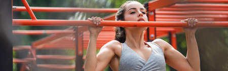 young athletic woman working out on pull up bar in outdoor gym, banner