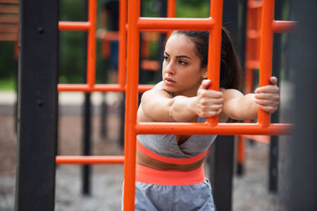 fit woman in sportswear exercising near orange vertical ladder outside
