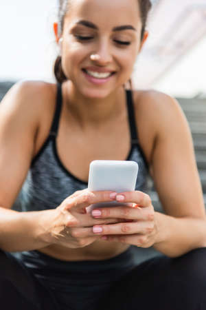 blurred and smiling sportswoman using smartphone outsideの写真素材