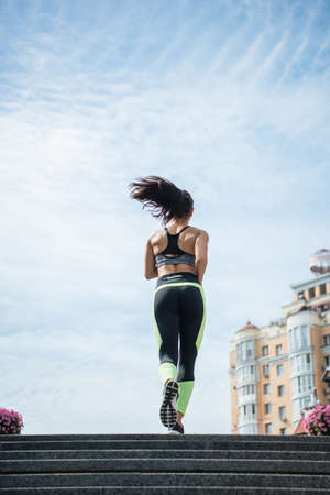 back view of sportive woman running on urban street