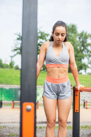 young and fit woman in sportswear exercising on parallel bars outside