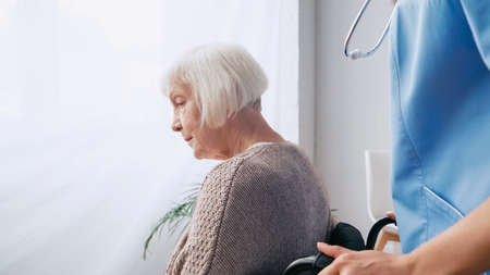 geriatric nurse with stethoscope moving aged woman in wheelchair