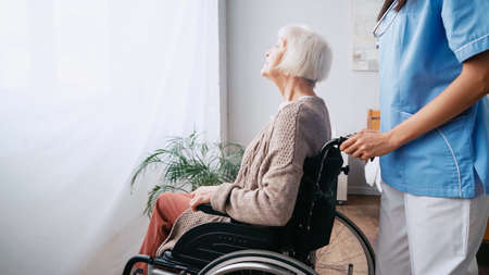 geriatric nurse moving aged woman in wheelchair