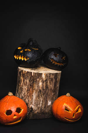 creepy and carved pumpkins on wooden stump and black backgroundの写真素材