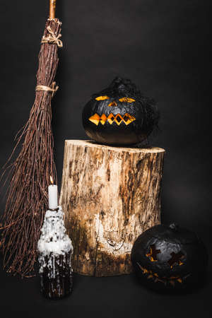 broom near dark pumpkin on wooden stump near burning candle on blackの写真素材