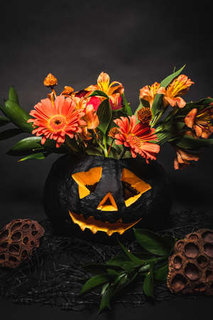 orange flowers with green leaves in spooky and carved pumpkin on black backgroundの写真素材