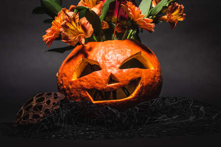 flowers in spooky and carved orange pumpkin on black backgroundの写真素材