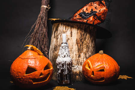 candle with wax and orange carved pumpkins near witch hat on wooden stump and black backgroundの写真素材