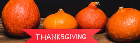 ribbon with thanksgiving lettering near orange pumpkins on wooden surface isolated on black, bannerの写真素材