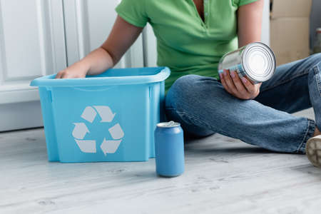 Cropped view of woman holding tin can near box with recycle sign on floorの写真素材
