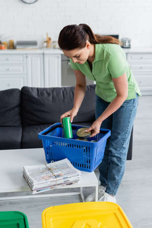 Woman holding cans near basket and newspapers in kitchenの写真素材