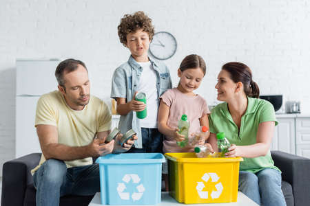 Smiling family sorting trash together in boxes with recycle symbolの写真素材