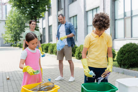 Children holding garbage near cans and blurred parents on urban streetの写真素材