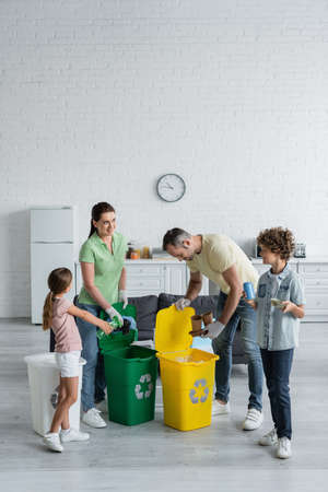 Cheerful family sorting trash in cans with recycle emblem at homeの写真素材