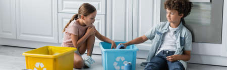 Kids putting tin cans in box with recycle sign in kitchen, bannerの写真素材