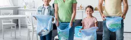 Smiling girl holding trash bag near parents and brother in kitchen, banner