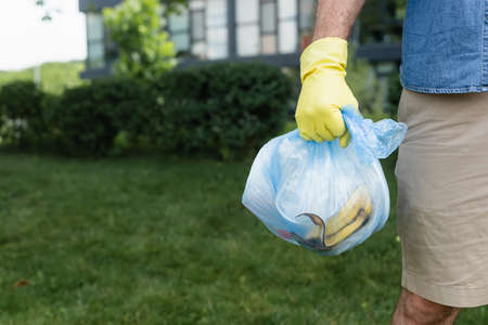 Cropped view of man in rubber glove holding bag with trash outdoorsの写真素材
