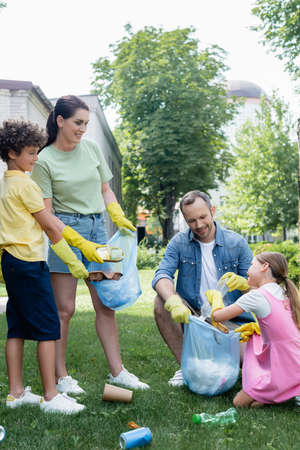 Happy children and parents in rubber gloves collecting trash on grassの写真素材