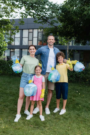 Happy family holding trash bags on lawnの写真素材